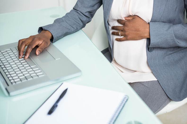 Pregnant woman holding belly and laptop at work - Pregnancy Discrimination